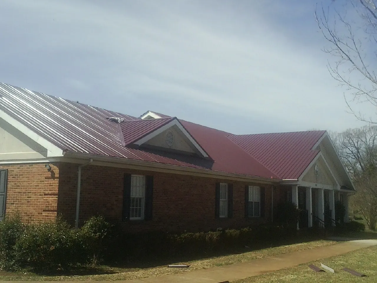 Red metal roof with gabled entries on a long brick building, from a Hail Damage Roof Repair job in Andale