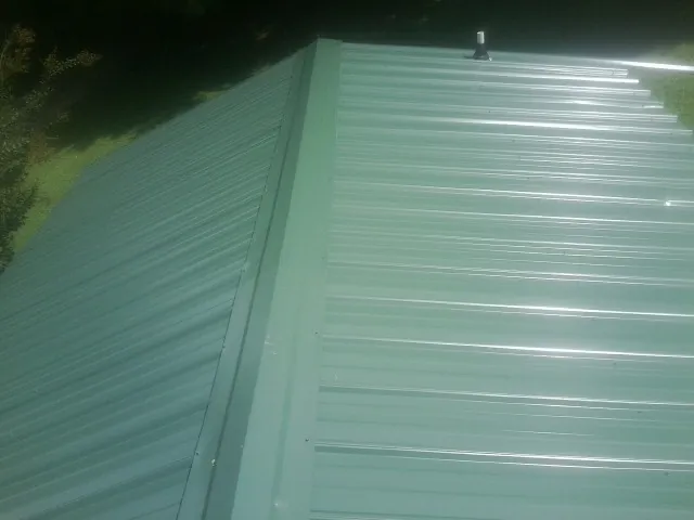 New green metal panels meeting at the ridge of a roof — Flat Roof Repair work by our crew in Andale