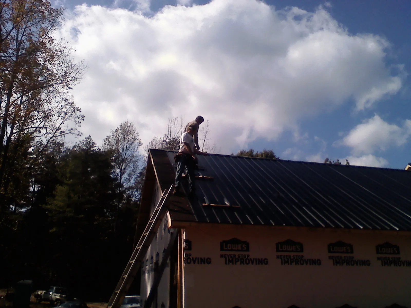 Roofer fastening dark metal panels high against a cloudy sky, from a Roof Inspection job in Andale